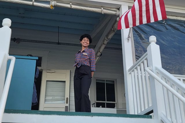 A participant poses at the entrance to the National Hotel in Block Island beside the American flag.