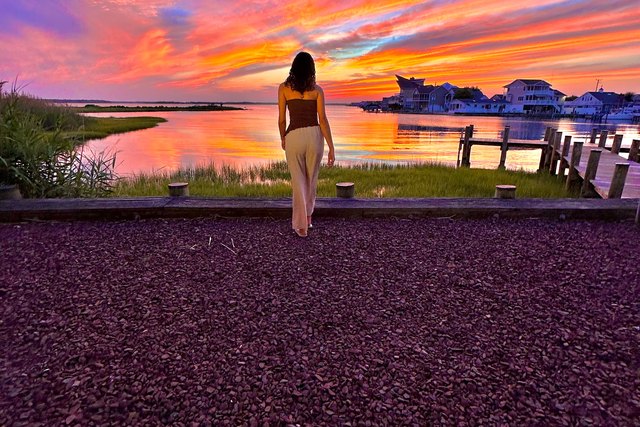 A young woman looks out at a colorful sky and the water at sunset in Ocean City.