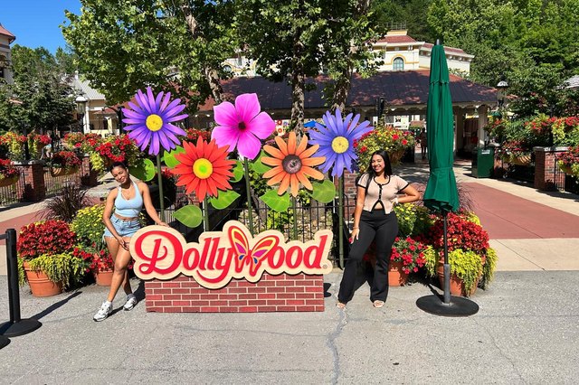 Two young women pose beside the Dollywood sign and its colorful flowers.