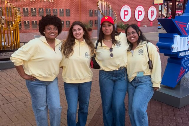 Four friends pose together in front of the Philadelphia Phillies wall.