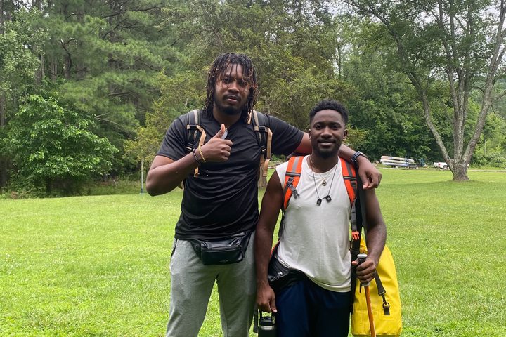 Two young people with backpacks and hiking equipment in a wooded setting, Summer Camp USA.