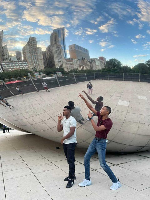 Dos jóvenes junto a la escultura reflectante Cloud Gate, con edificios al fondo.